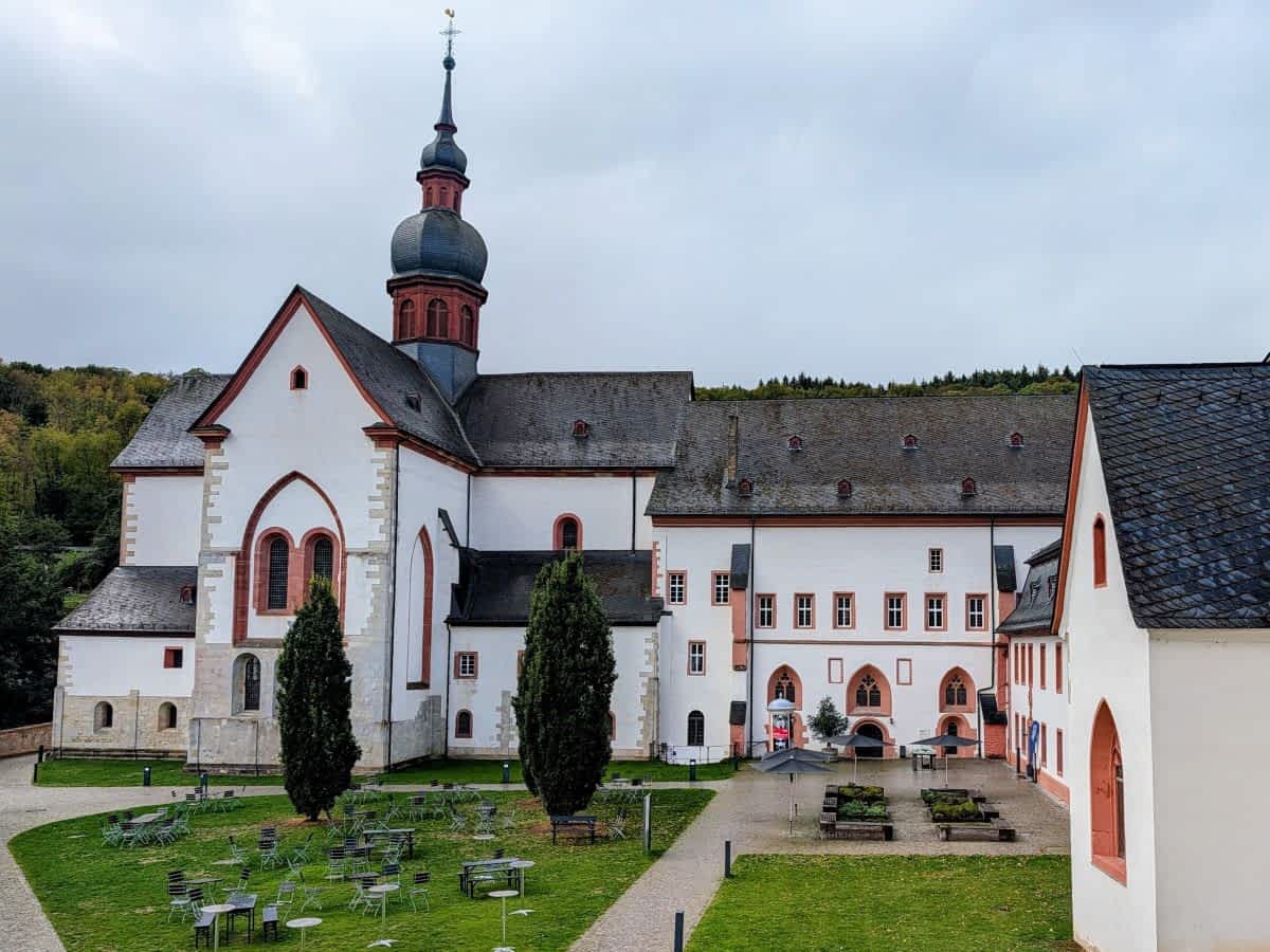 Außenansicht der historischen Klosteranlage Eberbach im Rheingau mit der imposanten Klosterkirche, weiß-roten Fassaden und einem gepflegten Innenhof mit Sitzgelegenheiten