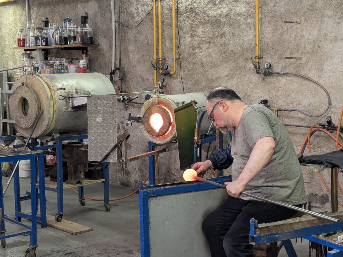 Ein Glasbläser in seiner Werkstatt in Kaysersberg bei der Arbeit mit glühendem Glas vor einem Schmelzofen. Ein Glasbläser in seiner Werkstatt in Kaysersberg bei der Arbeit mit glühendem Glas vor einem Schmelzofen.