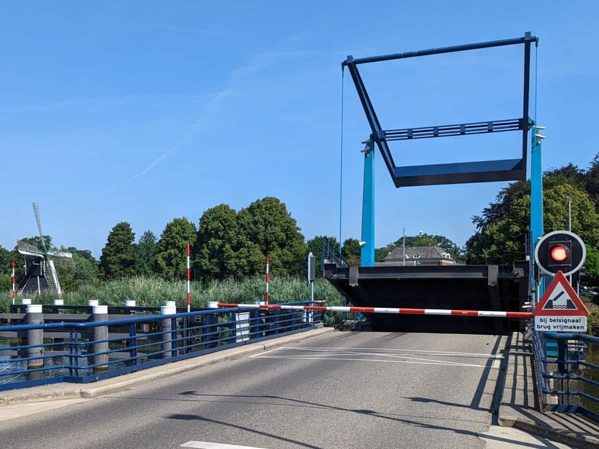 Blaue Hebebrücke über einen Kanal öffnet sich, im Hintergrund eine traditionelle Windmühle